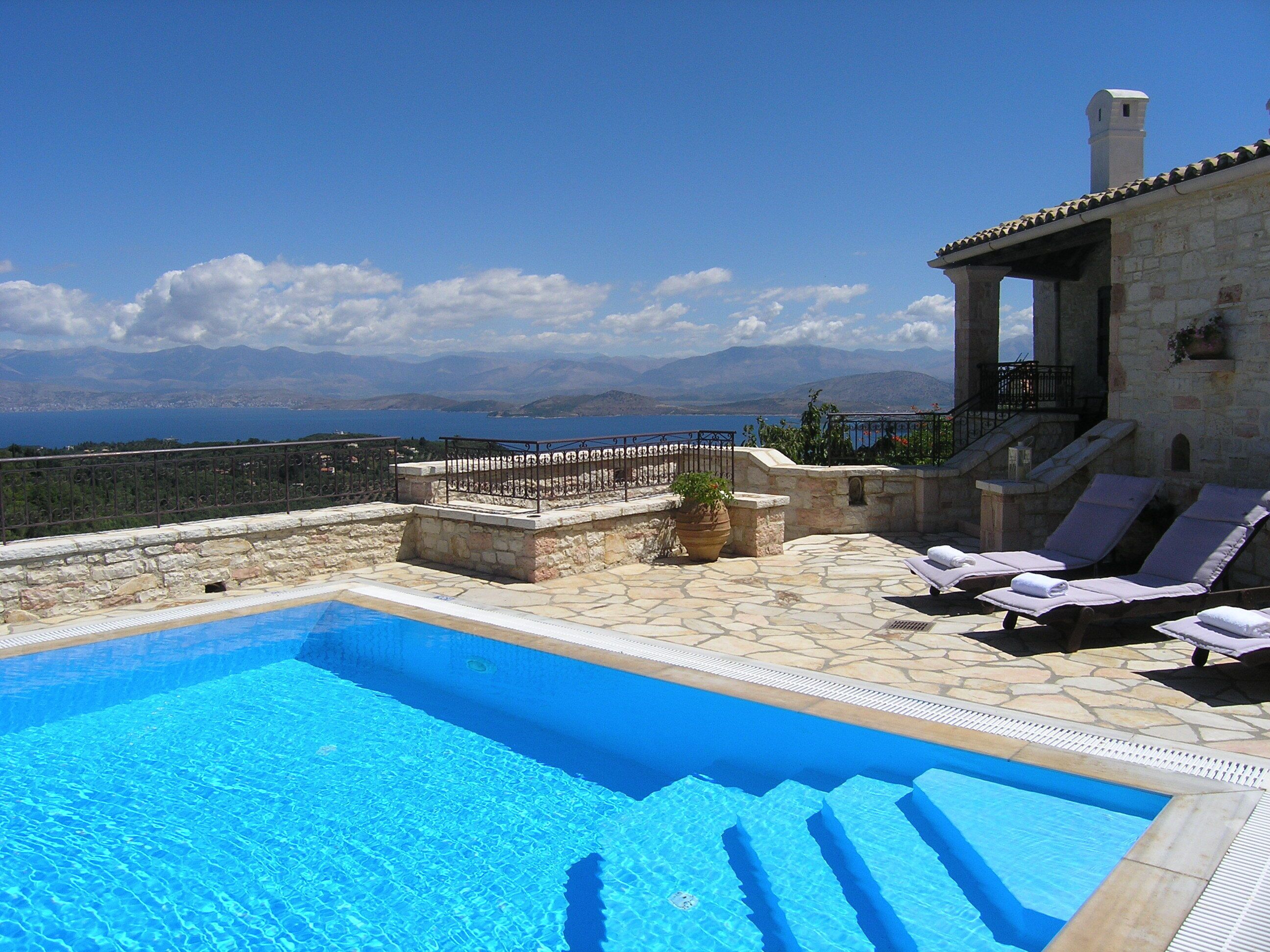 A pool with clear blue water, a stone deck, and lounge chairs.