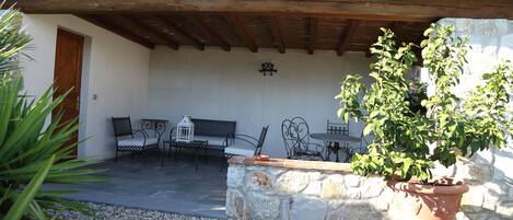 Un patio al aire libre con piso de piedra, una pérgola de madera y una zona de estar con sillas de metal y una mesa.