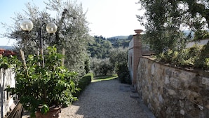A gravel path leading to a stone wall with a potted plant and two spherical street lamps. - Two-room apartment in old villa with pool located between Lucca and Florence (Pistoia)