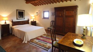 A bedroom with a bed, wooden headboard, two bedside tables with lamps, a wooden wardrobe, a chair, and a small table with a lamp. - Two-room apartment in old villa with pool located between Lucca and Florence (Pistoia)