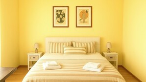 Una cama bien hecha con ropa de cama a rayas y dos almohadas, flanqueada por mesitas de noche con lámparas, en una habitación con paredes amarillas y obras de arte enmarcadas sobre la cama.