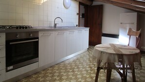 Eine Küche mit Herd, Spüle und Schränken, ein Esstisch mit Stuhl sowie ein Kühlschrank.