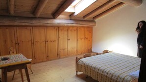 Ein Zimmer mit Holzboden, einem Bett mit gemustertem Überwurf, einem Holztisch mit Blumenmuster-Tischdecke und einem Holzschrank.