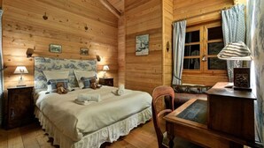 Una habitación acogedora tipo cabaña de madera, con una cama grande, un escritorio de madera y una ventana con cortinas.