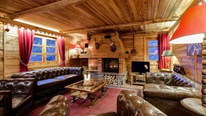 Interior de una cabaña de madera con chimenea, sofás de cuero, televisor y paredes de madera.