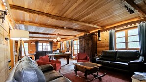 Acogedor interior de cabaña de troncos con mesa de billar, sofás de cuero y techo de madera.