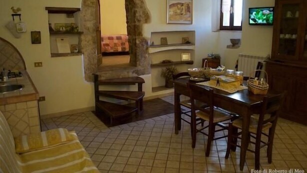 A cozy kitchen with a stone archway, a dining table with chairs, and a television on the wall.