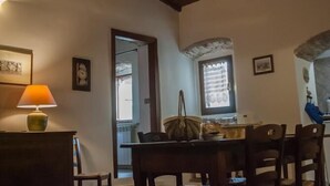 A dining area with a wooden table and chairs, a lamp, and a view of the kitchen through an archway.