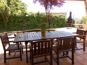 Un patio exterior con mesa y sillas de madera, rodeado de exuberante vegetación y una parrilla.