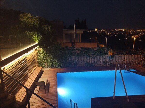 Vista nocturna de una piscina con una terraza de madera y escalones que bajan hacia ella.