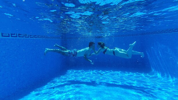 An underwater view of a swimming pool with two people swimming.