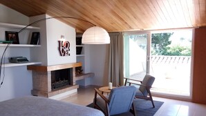 A bedroom with a fireplace, a bed, a chair, and a view of the outdoors.