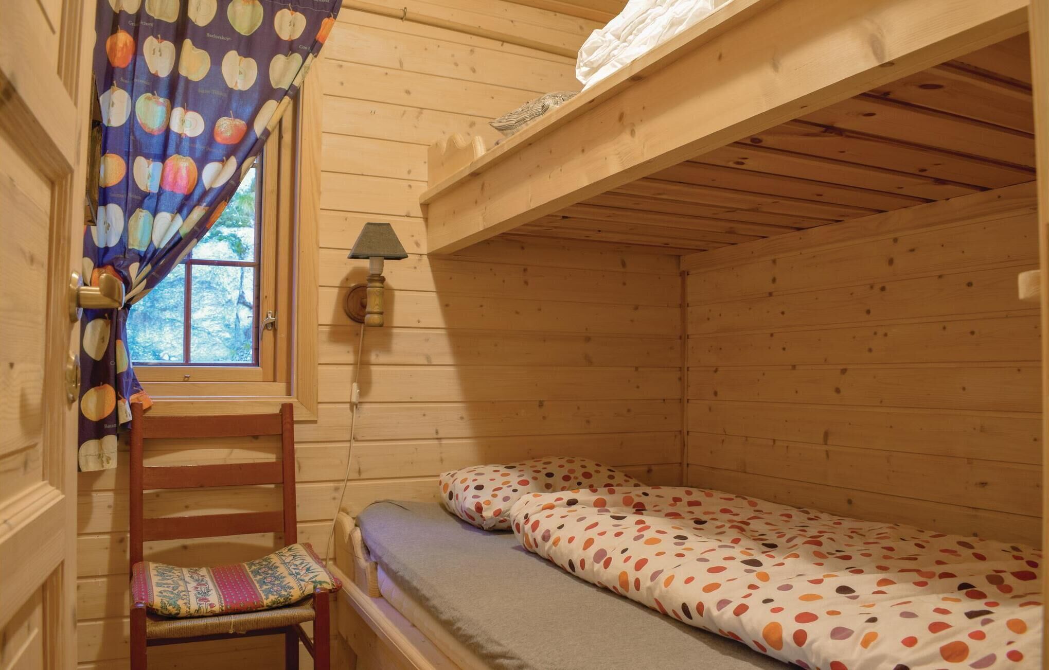 Habitació d'una cabana petita i acollidora, amb un llit individual, una cadira amb coixí, una finestra amb cortines i una làmpada penjada a la paret.
