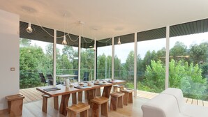 A modern dining area with a wooden table and benches, large windows offering a view of greenery, and pendant lighting. - Spectacular designer house, with heated pool, 8 minutes from the beach. (Ea)