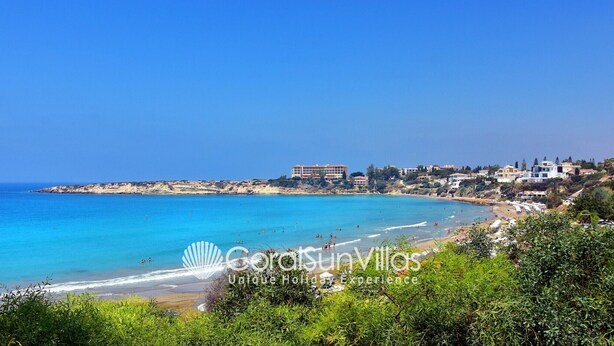 Vista costera con playa, mar azul cristalino y edificios al fondo.