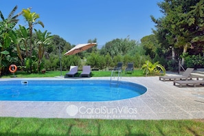 A swimming pool with lounge chairs and an umbrella, surrounded by greenery. - Huge Villa in the Heart of Coral Bay Paphos,100m to Beach Large Pool -Sleeps 15 (Pegeia)