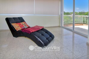 A black lounge chair with a red and orange cushion, a red throw blanket, and a view of greenery through a balcony door. - Huge Villa in the Heart of Coral Bay Paphos,100m to Beach Large Pool -Sleeps 15 (Pegeia)