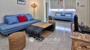 Una sala de estar moderna con un sofá azul, una mesa de centro de madera y otomanas de mimbre.