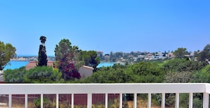A coastal view with a white railing, greenery, and buildings in the distance. - Huge Villa in the Heart of Coral Bay Paphos,100m to Beach Large Pool -Sleeps 15 (Pegeia)