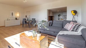 Un salon moderne avec un canapé gris, une table basse en bois et un coin repas comprenant un buffet blanc et des chaises.