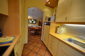 A kitchen with a tiled floor, wooden cabinets, a sink, and a dining area with a table and chairs.