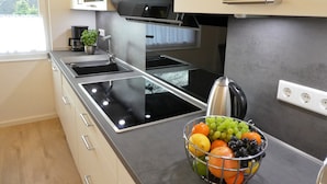Een moderne keuken met een ingebouwde kookplaat, een waterkoker en een fruitschaal op het aanrecht.