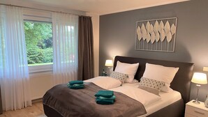 Een slaapkamer met een groot bed, twee nachtkastjes, een raam met gordijnen en een aan de muur hangend kunstwerk.