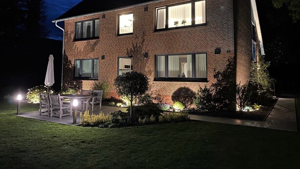 Een tweelaags bakstenen huis met een terras, buitenmeubilair en een goed verlichte tuin.