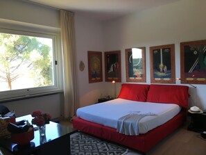Un dormitorio con cama, un escritorio con un florero y flores, una ventana con cortinas y decoración en la pared.