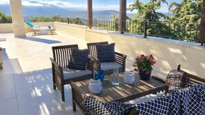 A terrace with wooden furniture, a table with drinks, and a view of mountains. - Villa LaMori in a quiet location with a heatable pool and a beautiful garden (Nikiforos Fokas)