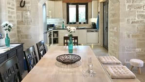 A kitchen with a stone wall, wooden beams, a chandelier, and a dining area with a table, chairs, and a vase of flowers. - Villa LaMori in a quiet location with a heatable pool and a beautiful garden (Nikiforos Fokas)