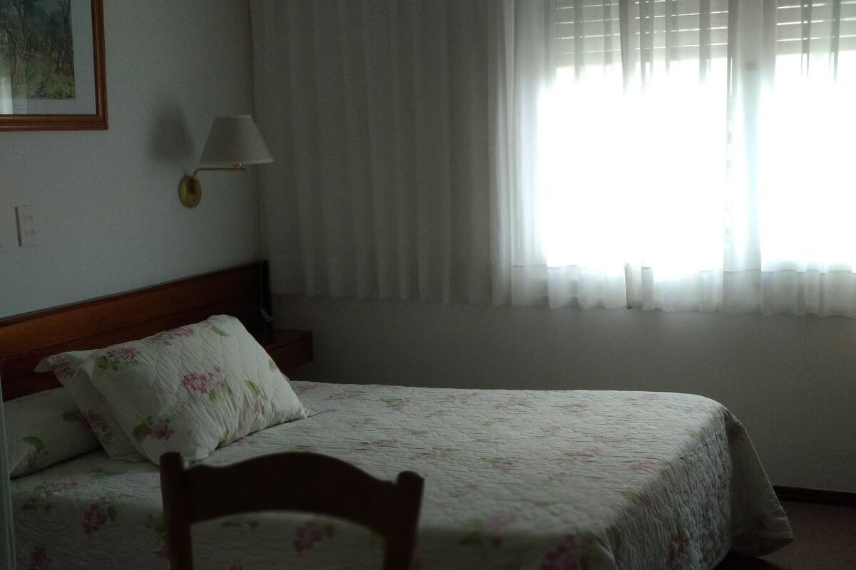 Una cama bien hecha con ropa de cama floral, un cabecero de madera y una lámpara de noche.
