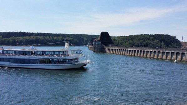 Une rivière où est amarré un grand bateau à un quai, un pont en arrière-plan et une colline boisée.