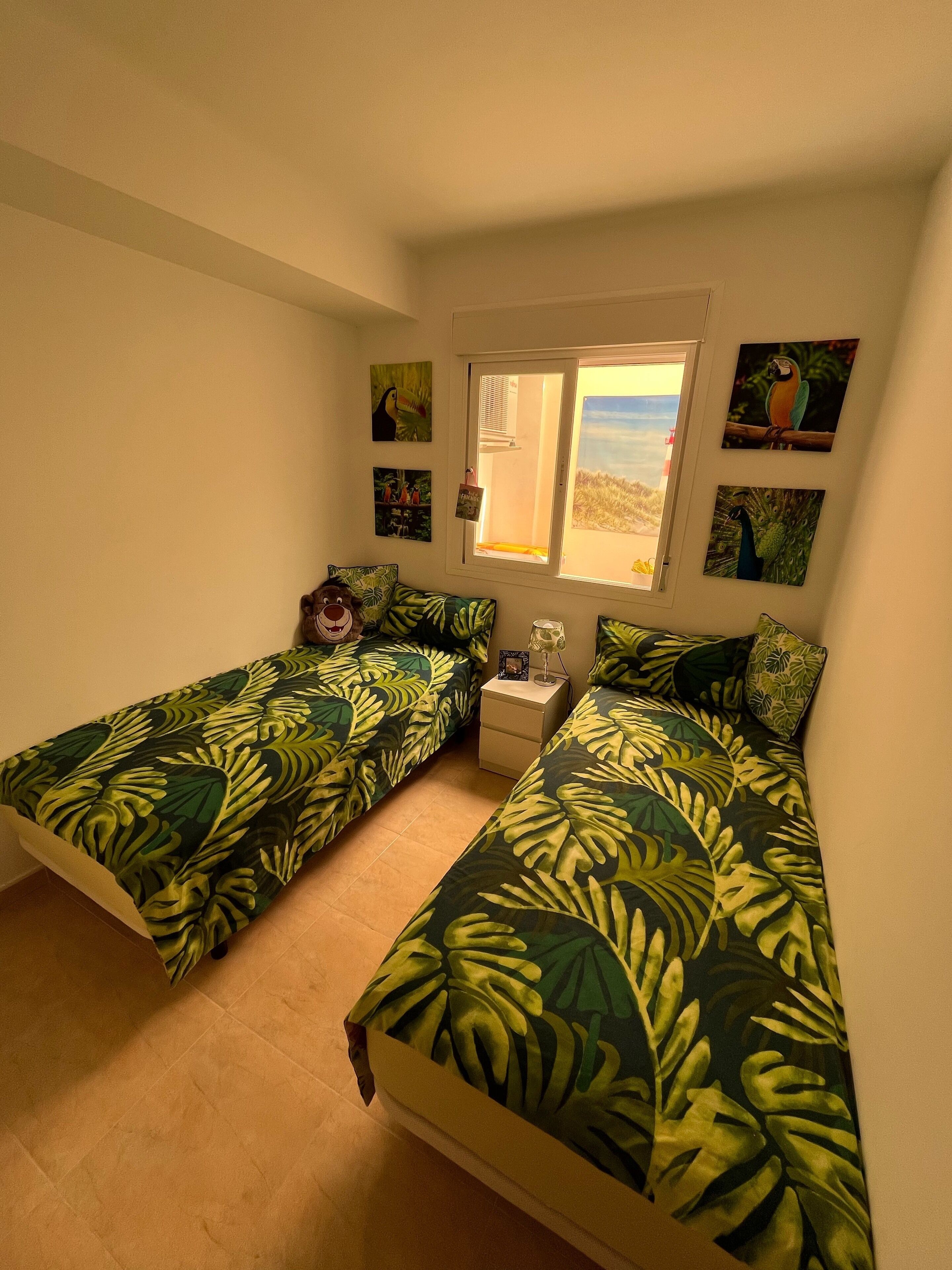 Un dormitorio con dos camas individuales, una mesita de noche, una ventana con vistas y decoración en la pared.