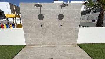 Un espace de douche extérieur moderne, doté de deux pommes de douche, d’un mur carrelé et d’une bordure d’herbe.