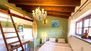 A bedroom with a bed, a wooden ladder, a chandelier, a surfboard, and a window. - Da Silva Surfcamp Areia Branca (Lourinhã)