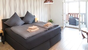 A modern bedroom with a large bed, dark bedding, and a view of the balcony. - Apartment waterfront (Waren (Müritz))
