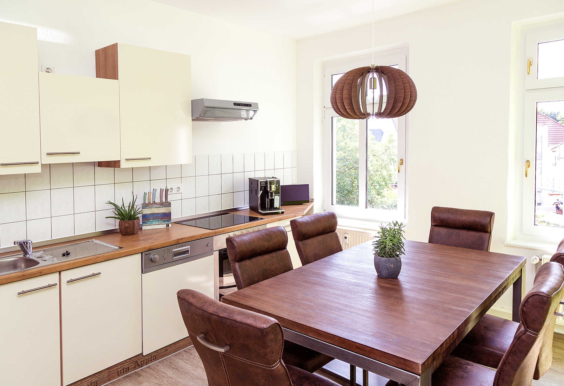 Une cuisine moderne avec des meubles blancs, un plan de travail en bois et un coin repas comprenant une table en bois et des chaises en cuir.