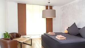 A modern bedroom with a large bed, a desk, two leather chairs, a hanging lamp, and a potted plant. - Apartment waterfront (Waren (Müritz))