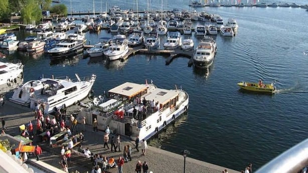 A marina with multiple boats docked, a ferry in the water, and people on the dock. - Apartment waterfront (Waren (Müritz))