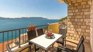 Un balcon avec une table dressée pour deux personnes, offrant une vue sur une étendue d’eau et des montagnes lointaines.
