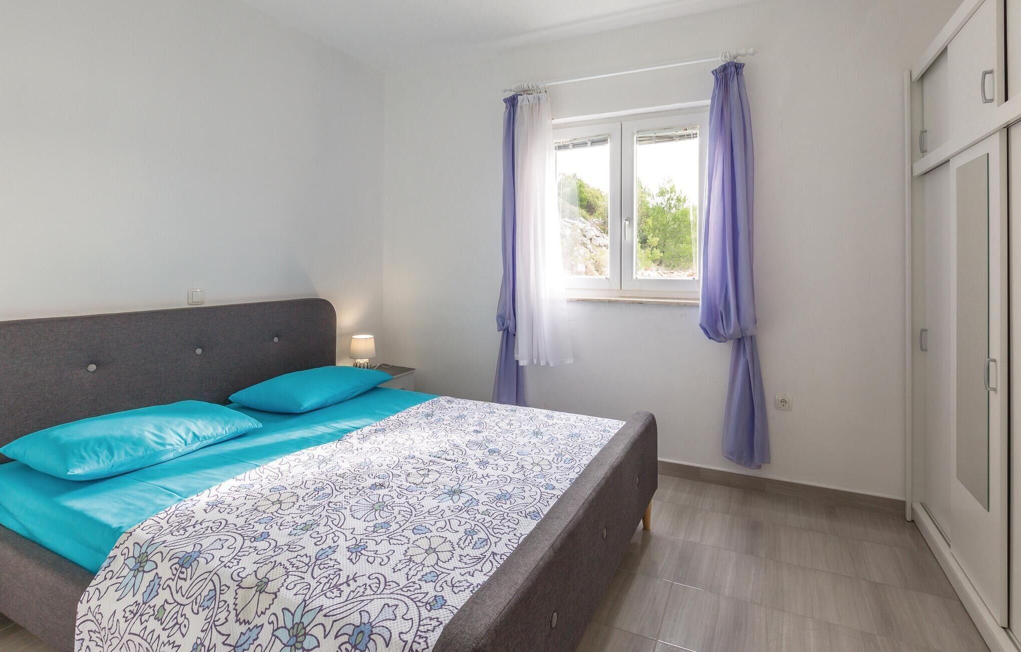 A bedroom with a bed, a nightstand, a window with curtains, and a wardrobe.