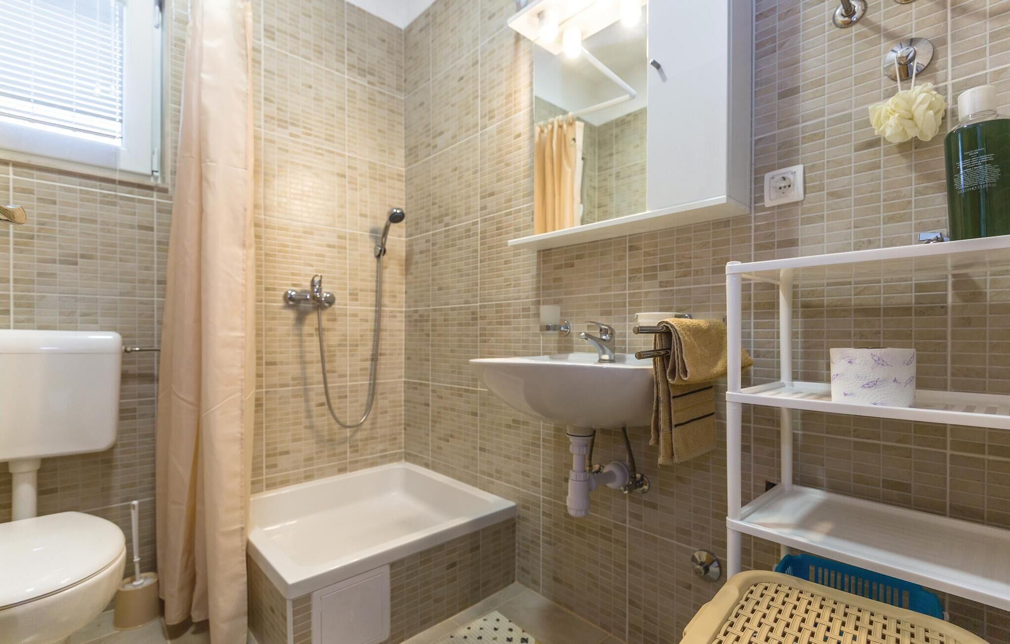 A bathroom with a toilet, shower, sink, and shelves.