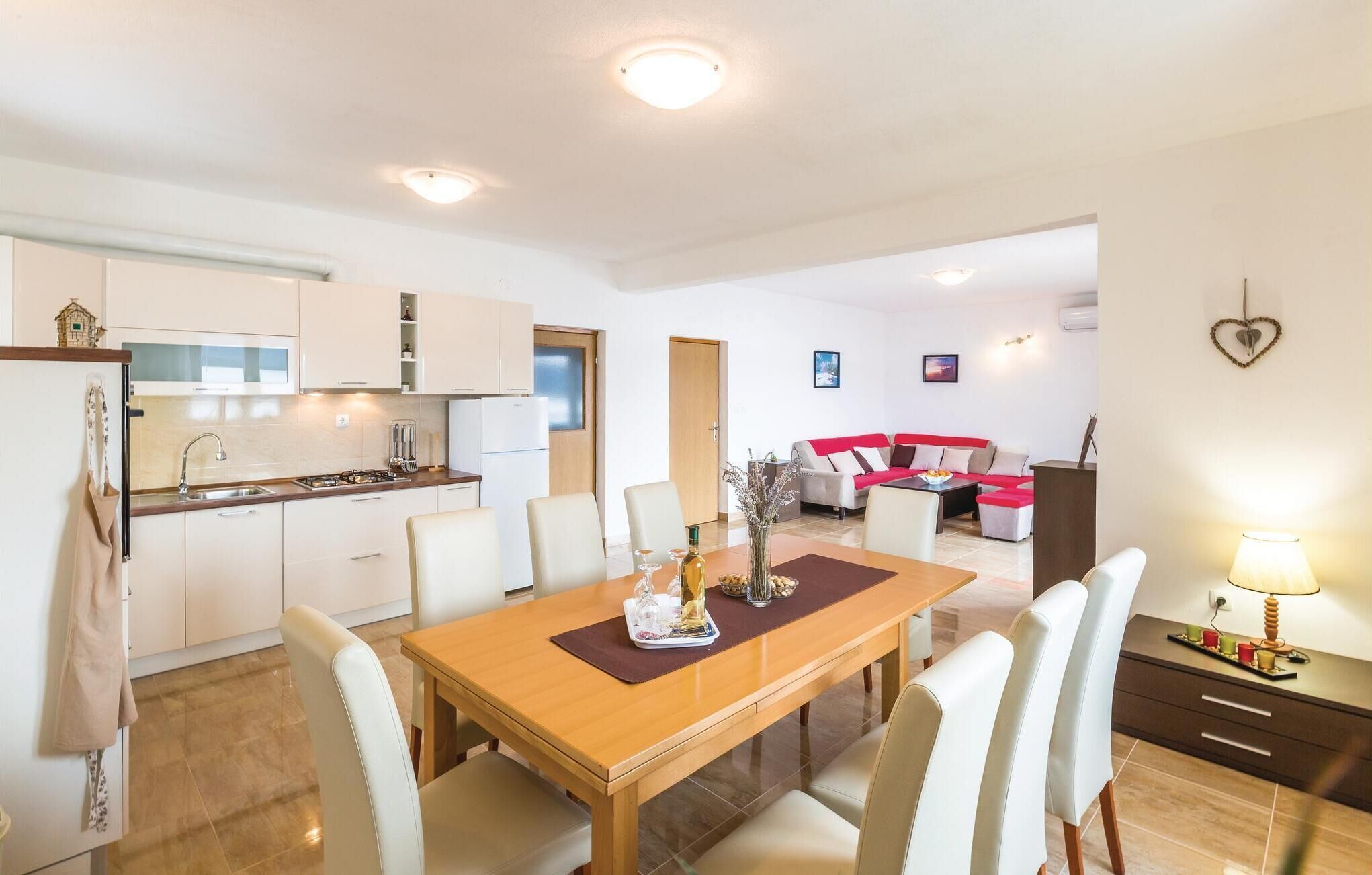 Une cuisine moderne avec des meubles blancs, une table à manger avec des chaises et un coin salon doté d’un canapé rouge.