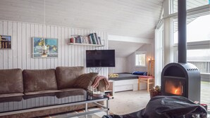 A cozy living room with a brown leather sofa, a flat-screen TV, a bookshelf, and a wood-burning stove. - 3 bedroom cozy home in Humble (Humble)