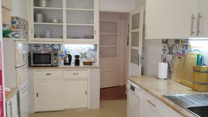 Une cuisine compacte avec des meubles blancs, un four à micro-ondes, une bouilloire et un lave-vaisselle. Elle est dotée d’un crédence carrelée et d’un plan de travail avec un évier.