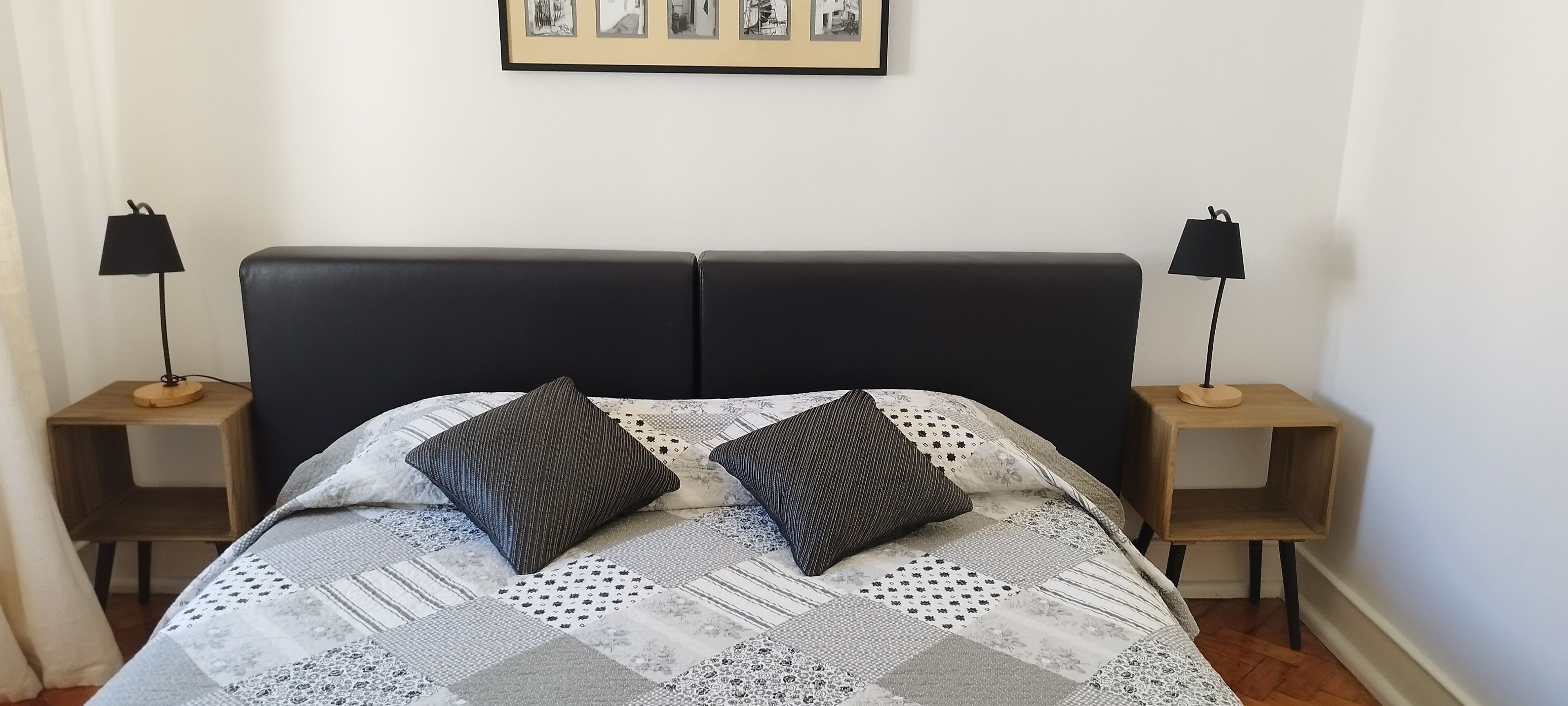 Ein ordentlich bezogenes Bett mit einer Steudecke, zwei Kissen und zwei Nachttischen mit Lampen.