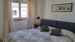 Une chambre à coucher comprenant un lit, une table de chevet, une lampe, une fenêtre avec des rideaux, un miroir et des tableaux encadrés accrochés au mur.