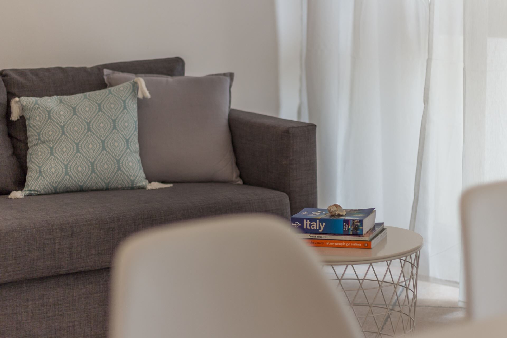 Una sala de estar moderna con un sofá gris, cojines estampados y una pequeña mesa redonda con libros.