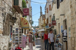A narrow street with shops and signs, including a pizza restaurant and a grill. - KATARINA 2 Apartment with a view of the sea, just 20 meters from the pebble beach (Mastrinka)